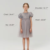 A young girl stands facing forward in the KIKI and JOJO Dusk Whisper Dress with silver shoes. Chest, hip, waist, and shoulder measurements are labeled. She is 55.51", 59.52lb, wearing size 9-10 years.